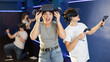 © JackF - Portrait of happy excited young girl with VR glasses on head, holding handheld controllers playing virtual reality game with friends..