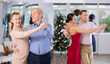 © JackF - Positive elderly man dancing elegant slow ballroom dance with younger female partner in stylish dress during New Year corporate party in office hall..