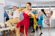 © JackF - Happy brunette in stylish red dress decorated with golden tinsel dancing energetic upbeat jive paired with cheerful male partner during New Year party in dance studio
