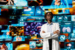 © DC Studio - Woman in white lab coat standing in front of digital health dashboards backdrop, analyzing human anatomy. African american scientist reviewing medical scans visualizations projected on videowall