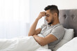 © Prostock-studio - A young Arab man sits on his bed with a pensive expression. He rests his forehead on his hand, deep in thought about his struggles. The room has soft natural light, enhancing the mood of reflection.