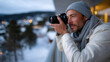 © Milos - A focused man looks through his camera lens, capturing the picturesque winter scenery, showcasing the beauty of the snowy landscape and the mood of creativity and exploration.