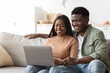 © Prostock-studio - A relaxed young African American couple spends their weekend at home on a comfy couch. They are enjoying each other's company while shopping or surfing the internet on a modern laptop.