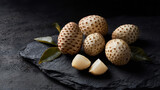 Whole and peeled salak snake fruit with fresh leaves on dark slate surface, exotic tropical fruit still life