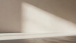 © FahVecStudio - Bright natural sunlight casts a strong diagonal shadow across a minimalist empty room's warm beige wall and textured floor, creating a serene, clean, and modern interior backdrop