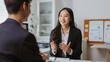 © amnaj - Asian businesswoman engaging in a positive conversation with a business partner during a meeting in a modern office setup