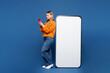 © ViDi Studio - Full body side profile view young happy woman she wear yellow sweater casual clothes big huge blank screen mobile cell phone with area use smartphone isolated on plain blue background studio portrait.