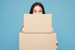 © ViDi Studio - Young woman she wear red striped sweatshirt casual clothes hold cover mouth with stack of two blank cardboard boxes isolated on plain pastel light blue background studio portrait. Lifestyle concept.