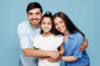 © ViDi Studio - Young smiling cheerful happy parents mom dad with child kid daughter girl wear casual clothes hug embrace posing look camera isolated on plain blue background Family day parenthood childhood concept.