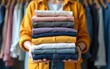 © Harper - Woman holding stack of clothes with used wardrobe, ready to give away. Circular fashion, fast fashion, clothing recycling, eco friendly sustainable shopping, resale, thrift stores concept. Wide banner