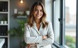 © Noah - Successful confident businesswoman at workplace inside office, woman with crossed arms smiling and looking at camera, standing near window. Satisfied office worker of company. High quality