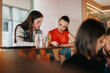 © qunica.com - Two colleagues sit at a cafe counter, focused on papers and a tablet. They discuss ideas with friendly expressions in a bright, modern setting, while other patrons blur in the foreground.