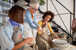 © luckybusiness - Teacher showing clay shaping to beginners on pottery workshop. Creative, hobby ,activities concept