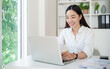© matinee - Happy young businesswoman working on a laptop in a bright home office.