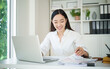 © matinee - Businesswoman analyzing financial reports and typing on laptop computer at modern home office.