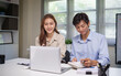 © matinee - Two young professionals working together at a desk, reviewing financial data on a laptop and calculator.