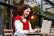 © Maria Vitkovska - Smiling woman working on laptop at outdoor cafe wearing casual red sweater
