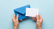 © smth.design - Hands holding blank white card and blue envelope on pastel background for message, invitation, announcement or greeting concept
