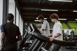 © m-art - Two young men focus on their workouts at a stylish gym. One jogs on a treadmill while the other looks out the window, enjoying the vibrant atmosphere and energy.