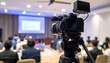 © Wool World - Professional video camera recording a business conference or educational seminar in a modern hall.