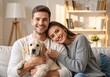 © Vasiliy - Portrait of a smiling young couple holding their golden retriever puppy. Happy family relaxing on the couch in a cozy home