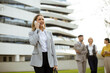 © BGStock72 - Businesswoman smiles while talking on phone outside modern office building during workday