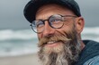 © Serhii - Joyful Bearded Man in Cap and Glasses Enjoying a Day at the Beach: A Close-Up Portrait in Nature