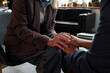 © TrueFrame Collective - Senior Caucasian woman comforting young adult Black woman by holding hands during therapy session, both seated in professional office setting, focus on supportive gesture