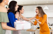 © JackF - Delighted surprised young woman in vibrant orange dress receiving unexpected gift from besties coming to celebrate birthday bash in cozy home setting with set table in background..