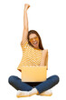 © Damir Khabirov - Happy young woman celebrating success with laptop, raising arms in excitement, sitting on floor