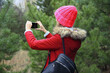 © rohappy - Young woman taking picture on phone Christmas tree in winter park, girl with smartphone in forest