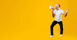 © Prostock-studio - A man wearing a santa hat is holding a megaphone while standing against a bright yellow background. He appears to be speaking or shouting, suggesting a festive celebration.