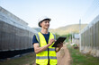 © bongkarn - Asian engineer man wearing safety vest and hard hat helmet write in tablet standing aside greenhouse