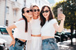 © halayalex - Three young beautiful smiling hipster female in trendy summer white t-shirt  and jeans clothes. Sexy carefree women posing in street. Positive models having fun, going crazy. In sunny day, take selfie