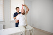 © Василь Івасюк - Physiotherapist guiding male patient with resistance band exercise for shoulder rehabilitation in clinic. Physical therapy session focused on injury recovery, strengthening, mobility improvement