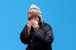 © Gatot - Man in winter clothes blowing his nose on a blue background, looking unwell