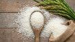© Yudi - Overhead shot of raw white rice grains scattered on a wooden table with a spoon, burlap sack, and fresh rice stalks. Healthy staple food