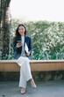 © Tj - Asian businesswoman smiling using smartphone in park
