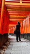 © Creativa Images - Female Tourist Walking Through the Vibrant Red Torii Gate Tunnel at Fushimi Inari Taisha