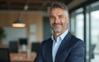 © Sophia - Positive confident mature executive man smiling and looking at camera while standing in office. High quality