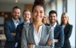 © George - A confident female business leader with his arms crossed, standing looking at the camera, with his team behind him, in an office environment. High quality