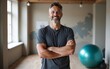 © George - Man, portrait and instructor with arms crossed in yoga class for ball exercise, posture training or balance technique. Mature coach, person and happy in pilates studio for fitness support or wellness