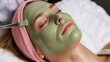 © SIDDQUE  - Woman with green clay face mask applying with brush in spa