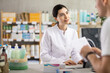 © JackF - Young professional female parmacist working computer and helping young guy with prescription in hand look for medicine in big drugstore