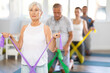 © JackF - Elderly woman doing pilates exercises with elastic band in group in fitness studio