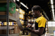 © DC Studio - African american male staff organizing packages on storage racks in a busy fulfillment center. Managing inventory with laptop and merchandise packed on racks. E-commerce order processing.