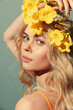 © VICHIZH - Beautiful woman with long blonde hair adorned with yellow flowers, exuding a serene and dreamy expression against a soft blue background.