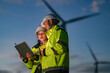 © ultramansk - Focused female and male engineers in safety gear using a laptop at a wind farm during twilight. Technical team collaborating on a green energy project for low-carbon power.