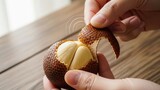 Close-up of hands peeling a ripe salak fruit, revealing its pale yellow flesh on a wooden table.