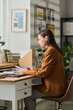 © pressmaster - Caucasian young adult woman sitting at desk in modern office setting, concentrating on paperwork with organized workspace and plants in background